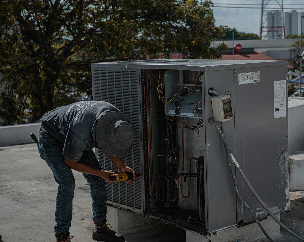 service-02 A technician is repairing an air conditioning unit on a rooftop, demonstrating skilled manual work.
