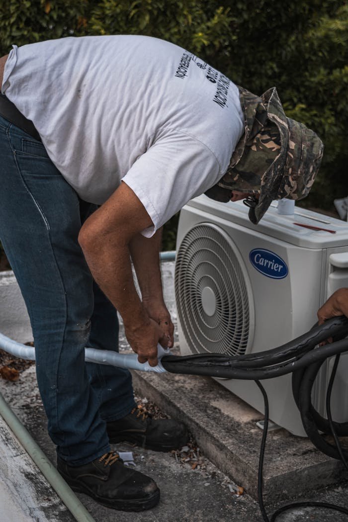 service-06 A technician performs maintenance on an outdoor air conditioning unit, focusing on hose connections.